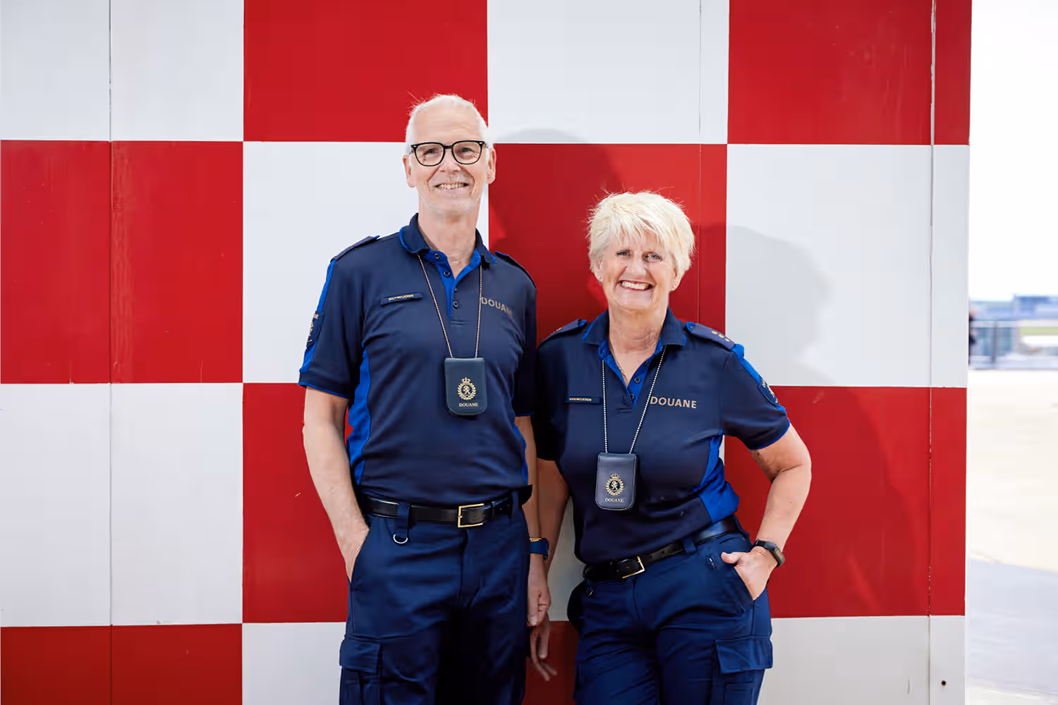 Kees en Caroline staan lachend dicht naast elkaar voor een wand met rood-witte vlakken.